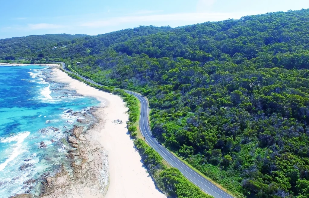 Aerial view of the Great Ocean Road coastline with winding road, beach, and turquoise ocean in Victoria Australia.
